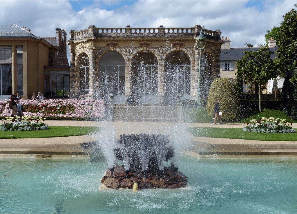 Fontaine devant bâtiment et fleurs.